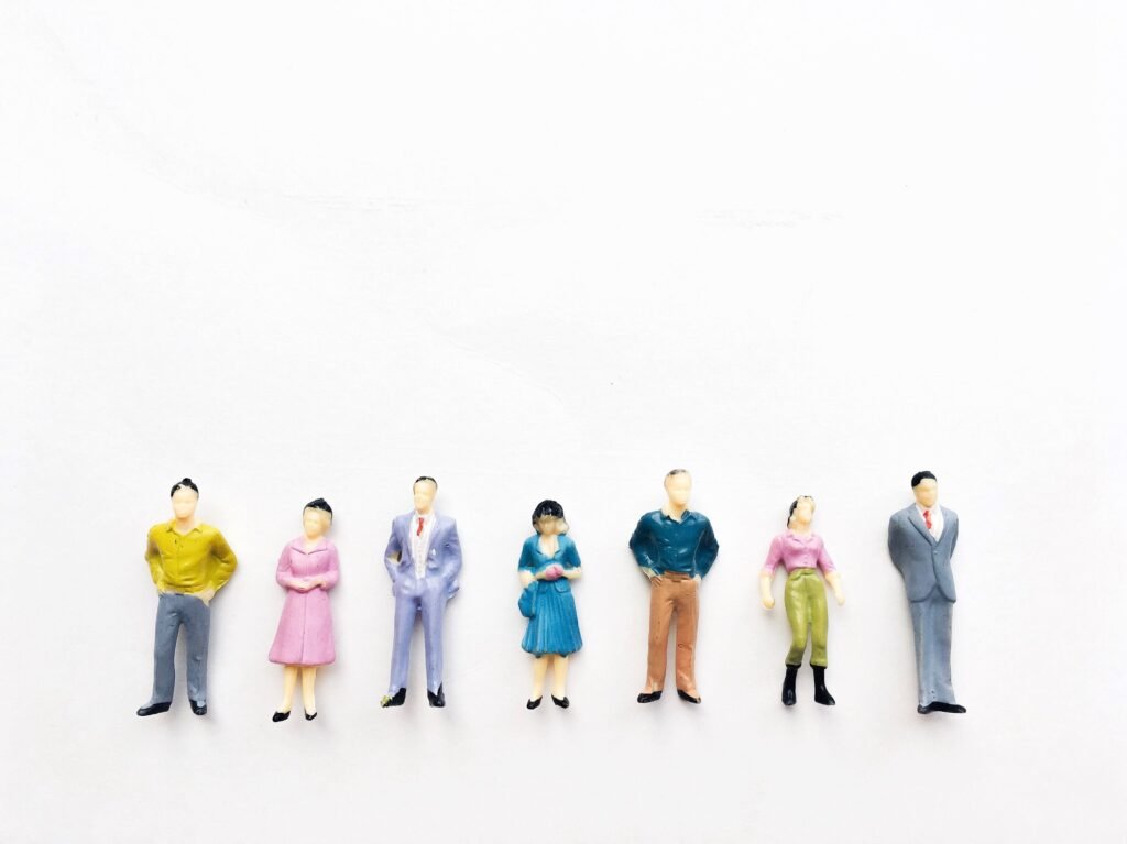 Horizontal row of seven tiny business people lined up on a white background.